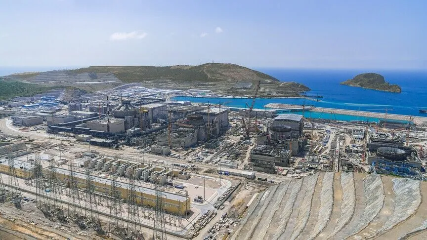 Aerial view of the Akkuyu Nuclear Power Plant under construction on Türkiye's Mediterranean coast, with reactor domes, cranes, and a switchyard beside the sea.